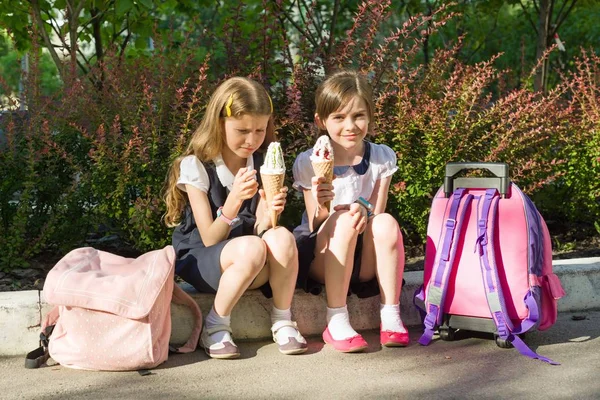 Retrato de dos novias colegialas 7 años en uniforme escolar con mochilas comiendo helado . — Foto de Stock