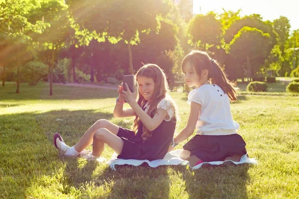 Веселые Маленькие Подружки Играют Смартфоном Сидя Лугу Парке Понятие Людей — стоковое фото