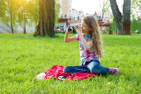 8岁小女孩看着相机坐在绿色草坪上的城市公园 — 图库照片