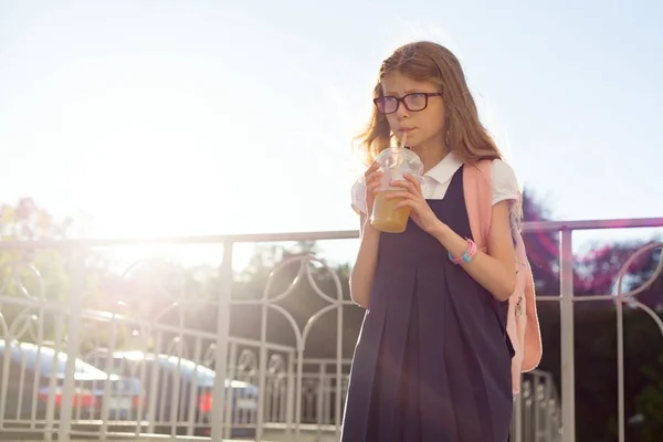 户外画像女孩小学生戴眼镜 用背包饮用天然果汁从玻璃 复制空间 — 图库照片