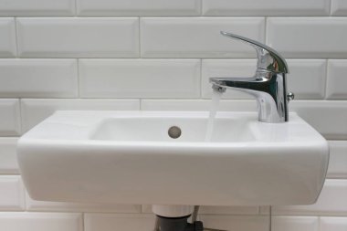 Close-up of white mini washbasin in the toilet with open chrome faucet washbasin. clipart
