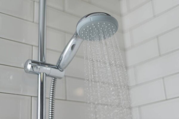 Close-up of chrome shower, faucet, in the bathroom covered decorative ceramic tiles with white glossy bricks. Water running from shower head.