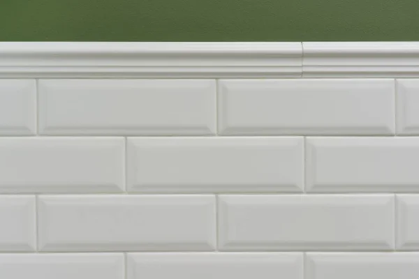 Green painted wall, part of the wall is covered tiles small white glossy brick, ceramic decorative molding tiles. Fragment of the walls of the bathroom, toilet, kitchen. Interior details close-up.