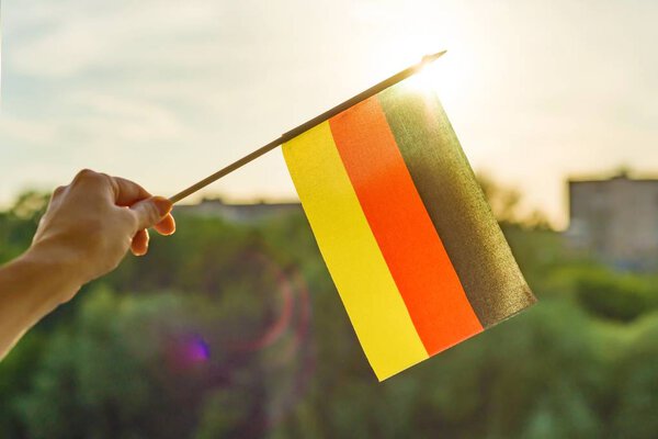 Hand holds Germany flag an open window. Background blue sky, silhouette of the city, sunset.