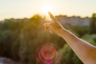 Gün batımına doğru işaret parmağı ile jest. Arka plan gökyüzü, şehir, gün batımı silüeti.