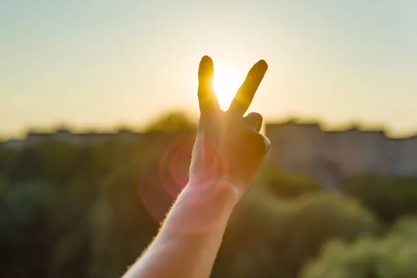 Hand showing two fingers or victory gesture. Background evening sunset, city silhouette.