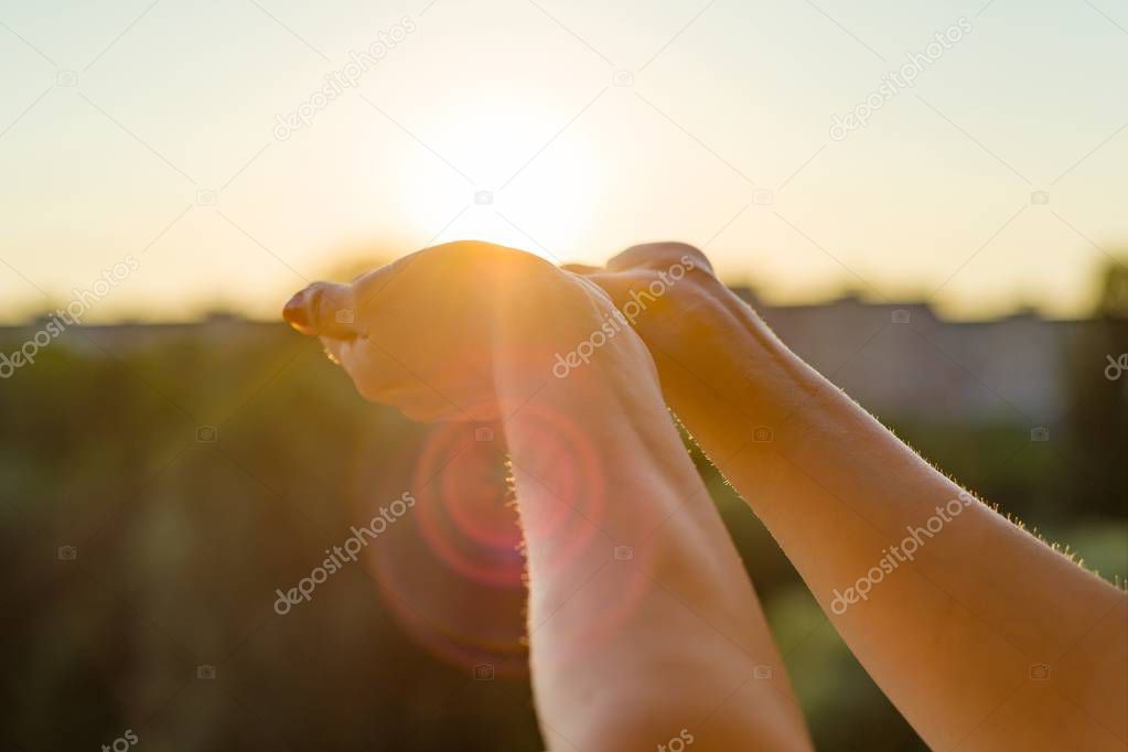 Hands open to the sunset, meditation, the background of the open window in the house, the silhouette of the city and the evening sun.