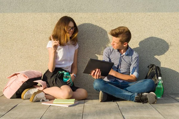 Okul çocukları gençler gri duvara yaslanın, ders kitapları okumak, su içmek, tablet vasıl bak. Kız tablet vasıl arıyor ve harika bir fikir, işaret parmağı işaret bulmak
