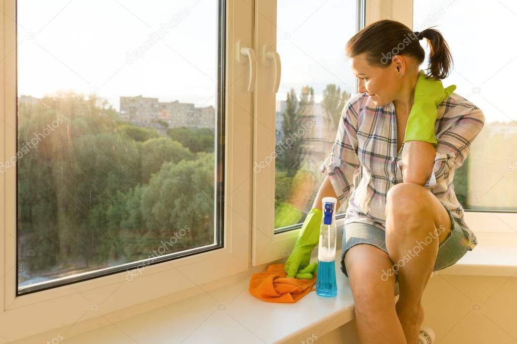 Female with rubber protective gloves, rag and sprayer detergent looks into a clean washed window