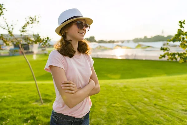 户外肖像的年轻女孩在太阳镜和帽子与武器交叉 背景绿草 游憩区 夏季日落 复制空间 — 图库照片