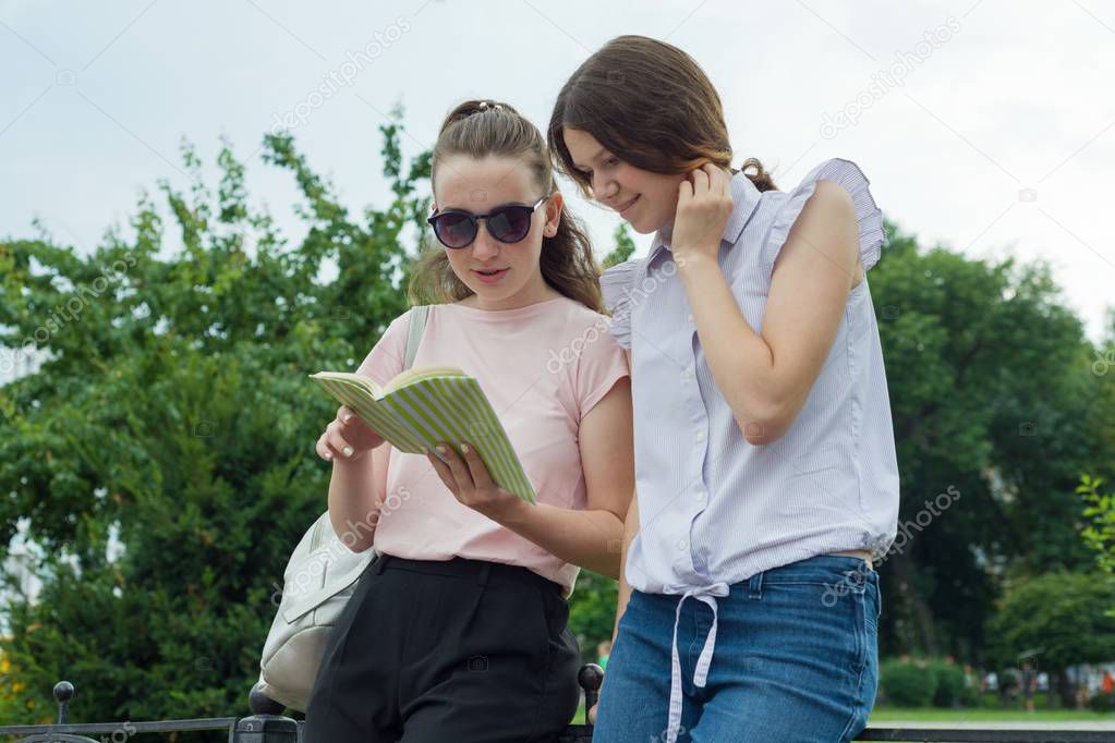 Two learning girls students with backpacks and textbooks outdoor in a park