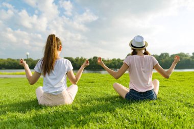 İki genç kız parkta, gün batımında yoga Yoga poz açık, yapıyor arkadan görünüm