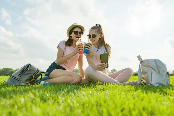 青少年女孩在帽子和太阳镜在休闲公园的绿色草坪上享受他们的鸡尾酒 — 图库照片