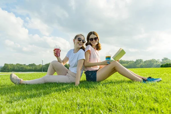 夏日阳光明媚的一天 两个女朋友少年坐在绿草地上 喝鸡尾酒 玩得开心 — 图库照片