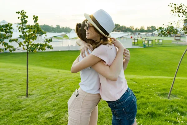 The friendship of two teenage girls, best girlfriends have fun in nature, on the green lawn of recreation park and entertainment. Embrace the greeting and parting