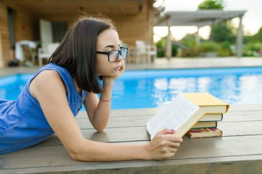 Kitap okuma genç kız gözlük ile bir yığın kitap, havuz kenarında. Eğitim, yaz, bilgi