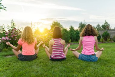 Genç Genç kız pratik yoga Grup, meditasyon, çim evin yanında bir lotus pozisyonda oturmak.