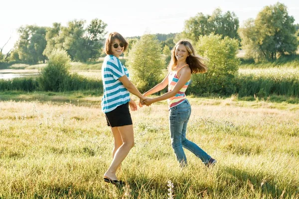 Happy mom and teen daughter smiling holding hands on nature on a sunny summer day — Stock Photo, Image