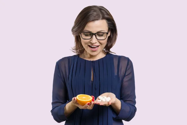 A mulher tem vitamina natural laranja em uma mão e vitamina C sintética na outra. Faz uma escolha. — Fotografia de Stock