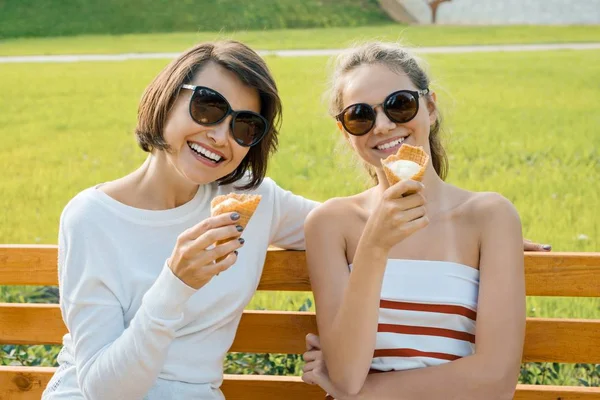 Happy family weekend, outdoor portrait of mom and daughter with ice cream in the park on a bench
