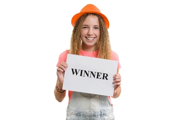 Winner text message written on white paper in hands pretty young teen girl, smiling girl in hat on isolated white background — Stock Photo, Image