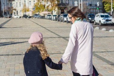 Anne ve kızı çocuk el ele, yürümek ve şehrin sokak konuşmak, arkadan görüntülemek
