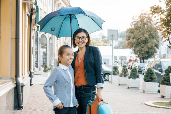 Открытый портрет улыбающейся матери и дочери под зонтиком. Мать и девочка с рюкзаком по дороге в школу — стоковое фото