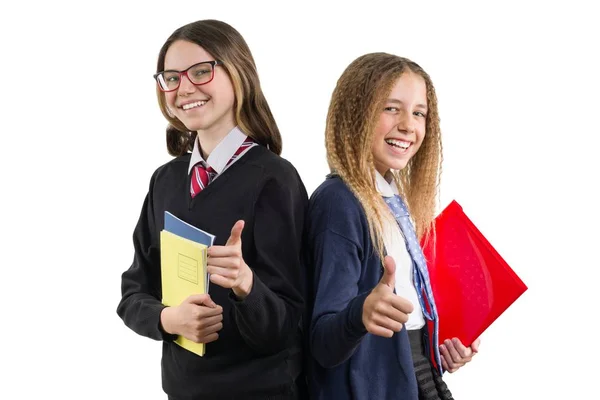 Due ragazze sorridenti del liceo in uniforme indossano occhiali con quaderni che mostrano pollice su segno ok, posa su sfondo bianco, isolato — Foto Stock