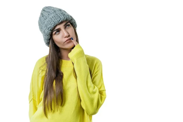Mujer hermosa joven en suéter amarillo y gris grande lazo gorro de punto, reflexivo sosteniendo un dedo cerca de sus labios, sobre fondo blanco aislado —  Fotos de Stock