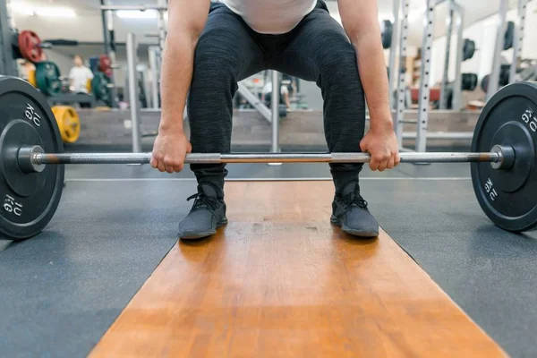 Primer plano de los brazos y las piernas del hombre haciendo ejercicio con barra de pesas en el gimnasio deportivo. Atleta, culturismo, entrenamiento, levantamiento de pesas, concepto de ejercicios de entrenamiento — Foto de Stock