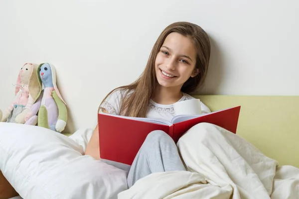 Dívka 10 let sedí doma v posteli s školní notebook, čtení a učení se, příprava na školu doma — Stock fotografie