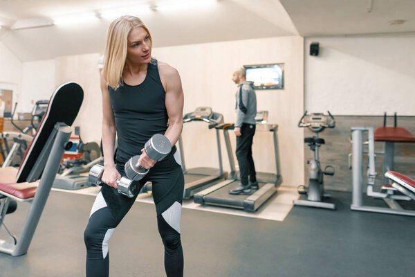 Young beautiful blond woman doing strength exercises with dumbbells in gym. Sport, fitness, bodybuilding, training, workout exercises concept