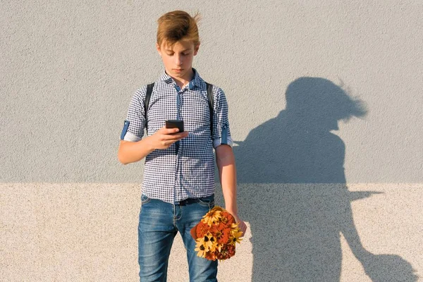 Εξωτερική πορτραίτο του έφηβου αγοριού με μπουκέτο από λουλούδια, ανάγνωση κειμένου σε smartphone, γκρι φόντο τοίχο αντίγραφο χώρου — Φωτογραφία Αρχείου