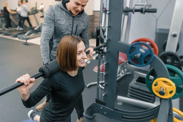 Entrenador de fitness personal masculino que ayuda a las jóvenes a hacer ejercicio en el gimnasio. Deporte, atleta, entrenamiento, estilo de vida saludable y concepto de personas — Foto de Stock