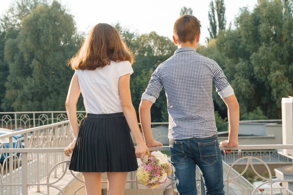 Tonåring unga par pojke och flicka stående rygg, solig sommardag, flicka håller blombukett i handen — Stockfoto