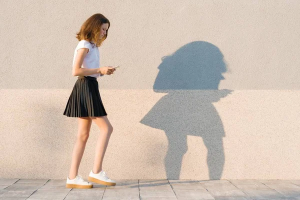 Chica joven caminando con grandes pasos y leyendo texto en el teléfono móvil, fondo de pared al aire libre gris, espacio de copia —  Fotos de Stock