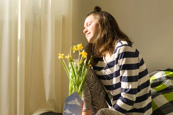 Nastolatek dziewczyna z bukietem żółte jare kwiecie, uśmiechnięta i szczęśliwa siedząc w domu w łóżku — Zdjęcie stockowe