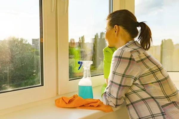 Adult woman washes windows, cleaning the house, female looks into a clean washed window — Stock Photo, Image