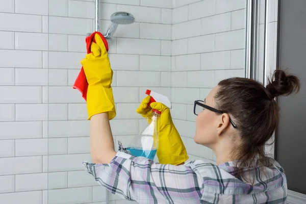 Уборка дома. Женщина чистит ванную, женщина в повседневной одежде с моющим средством и мочалкой у себя дома в ванной комнате — стоковое фото
