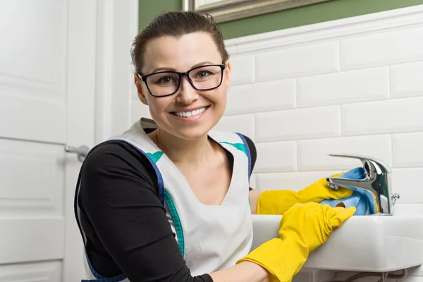 Портрет усміхненої дорослої жінки в окулярах, гумові рукавички роблять прибирання будинку, прибирання жінок ванна кімната — стокове фото
