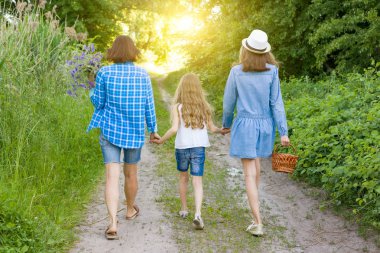 Aile Orman kırsal yolda yaz aylarında. Anne ve kızı el ele, arkadan görüntüleme.