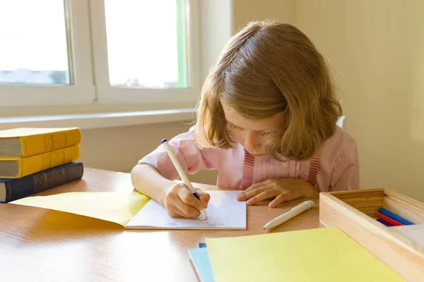 Colegiala, niña de 8 años, sentada a la mesa con libros y escribiendo en cuaderno. Escuela, educación, conocimiento y niños — Foto de Stock