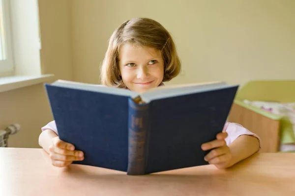 Μικρό κορίτσι φοιτητής κάθεται σε ένα γραφείο με το βιβλίο. Σχολείο, παιδεία, γνώση και παιδιά — Φωτογραφία Αρχείου