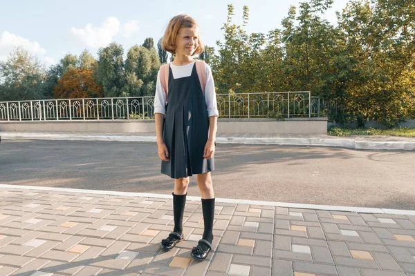 Retrato al aire libre de un estudiante pequeño, chica con gafas, uniforme con mochila. Escuela, educación, conocimiento y niños —  Fotos de Stock