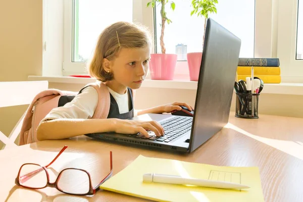 Маленька студентка 8 років у шкільній формі з рюкзаком використовує комп'ютерний ноутбук. Школа, освіта, знання та діти — стокове фото