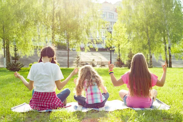 Tre unga flickor gör yogaställning utomhus, yoga i solnedgången i parken, bakifrån — Stockfoto