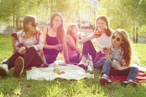 Odpočívej v parku. Matky s dětmi sedět na trávě, ženy pijí kávu, děti jedí jablka. — Stock fotografie