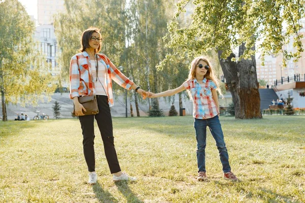 Mom and daughter holding hands walking in the park, golden hour