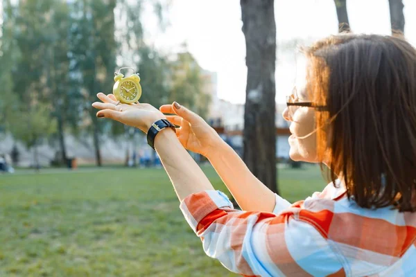 Reloj despertador en mano femenina, hierba verde de fondo en el parque, luz solar, espacio para copiar — Foto de Stock