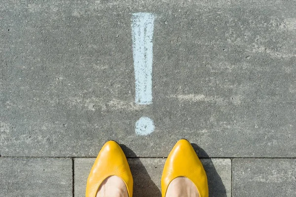 Female feet with exclamation point, symbol of attention drawn on the asphalt